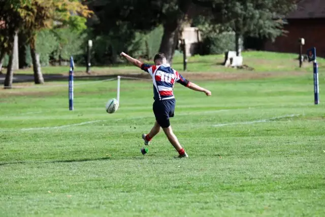 A Sixth Form boy kicking a rugby ball on the pitch.