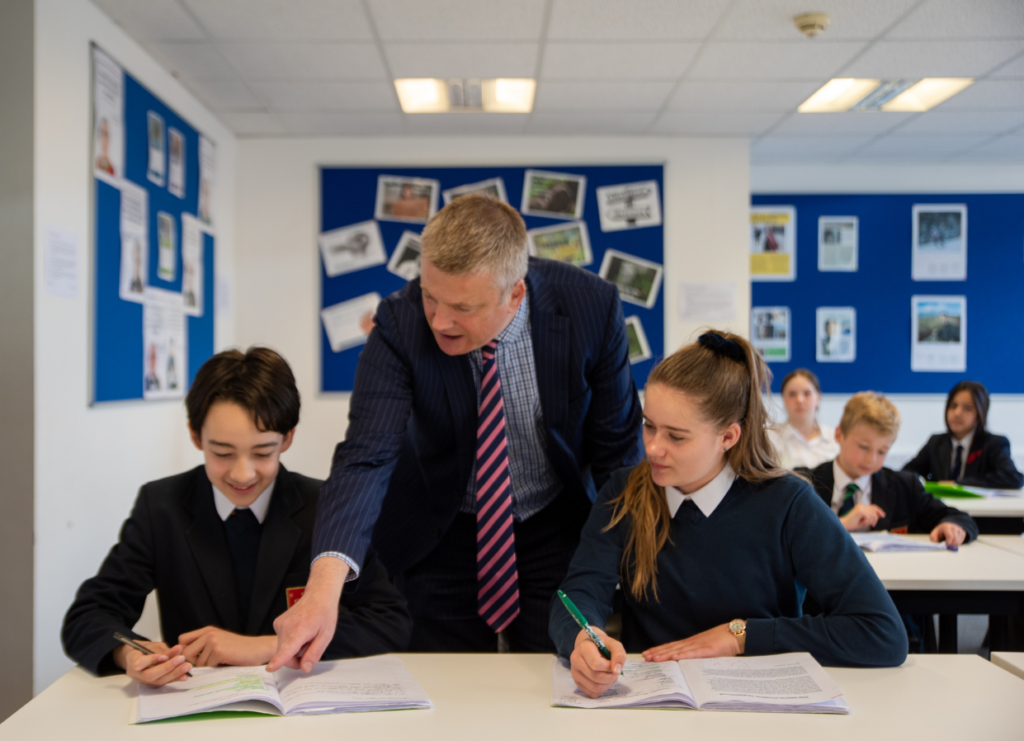 A male teacher assists a boy and a girl in class