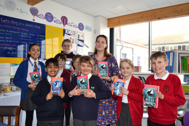 Pupils from four different schools stand with author, Alex Foulkes, as they all hold up one of her books.