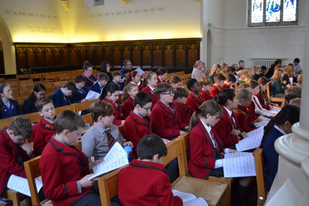 Rows of pupils sitting down in the Chapel reading song lyrics.