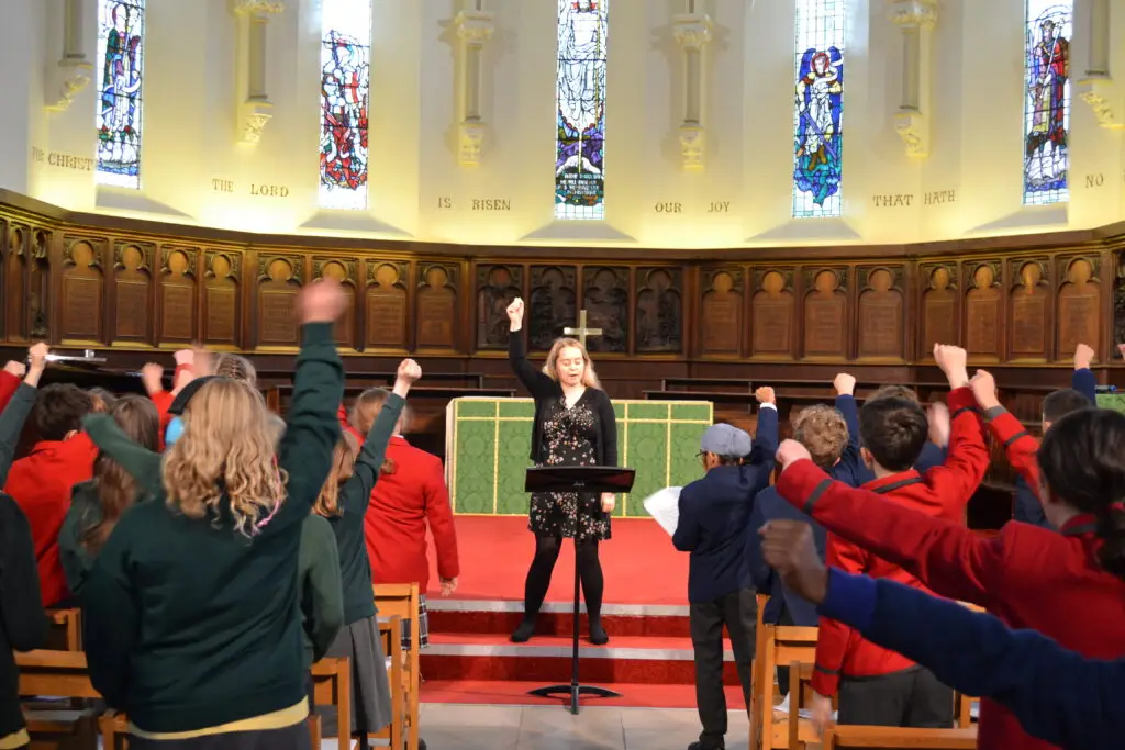 A teacher standing at the front of the pupil instructing the pupils on how to perform actions during a song.