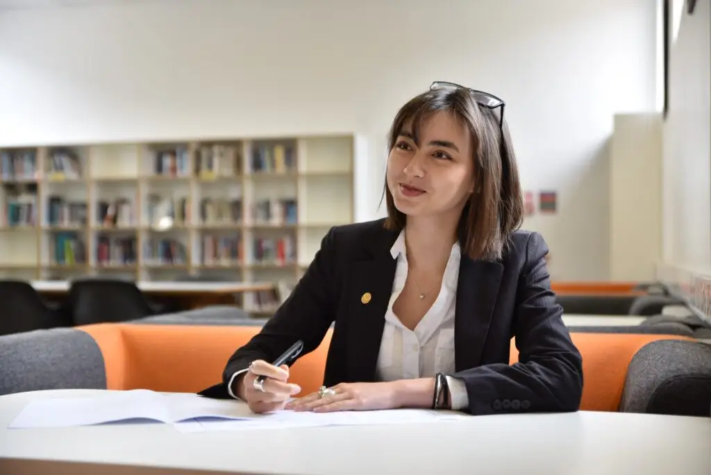 A female Sixth Form student smiling whilst working at a desk in the Wortley Resources Centre.